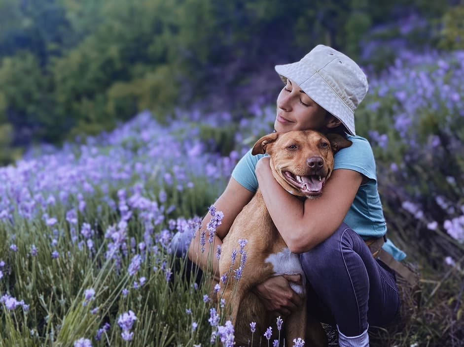 Lady loving a dog in field of flowers